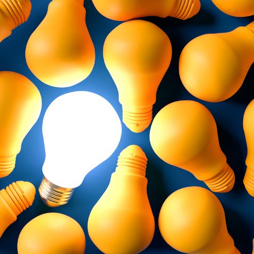 Lit light bulb laying among unlit yellow bulbs on blue background.